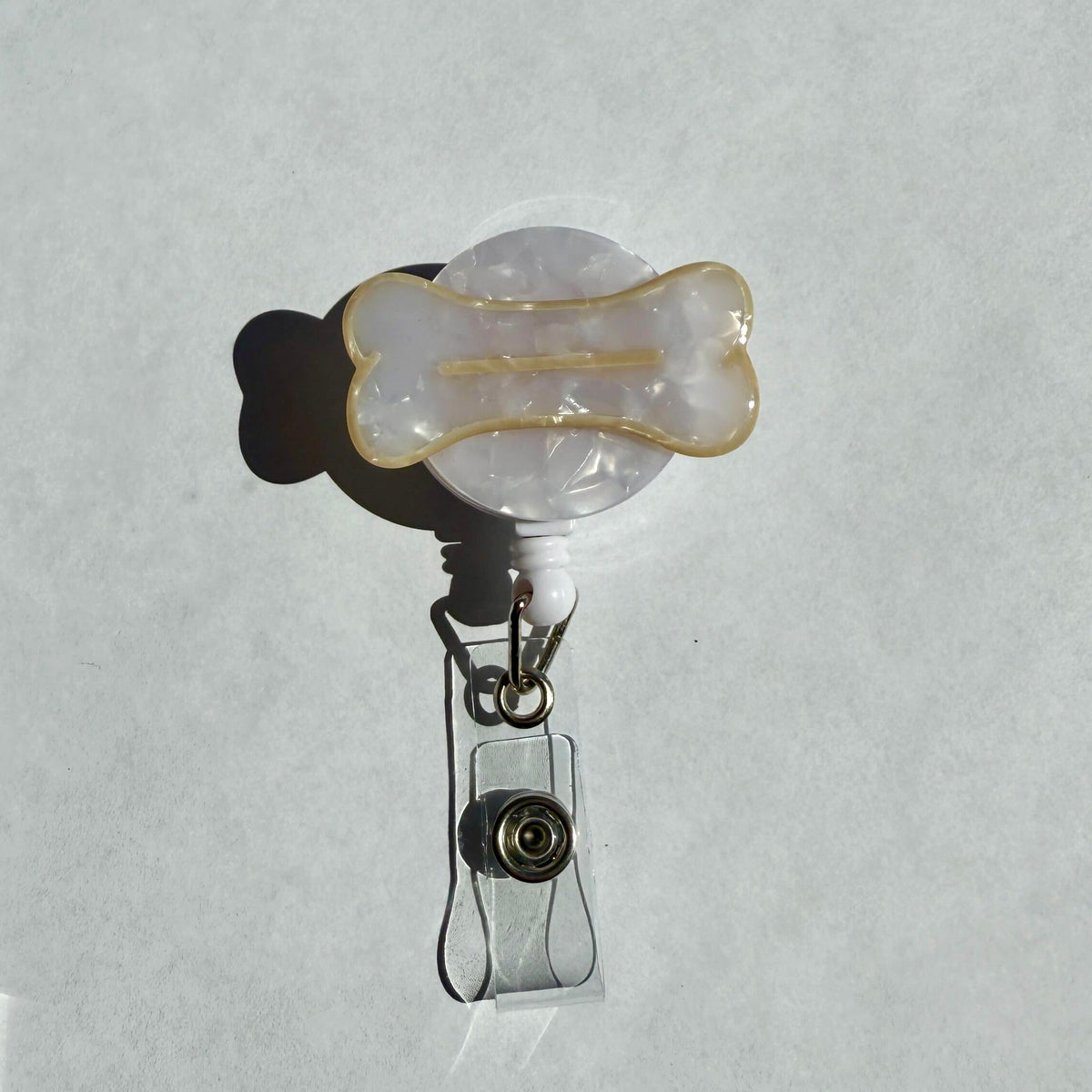 A badge reel with a bone design on a white background. The bone is white with a beige outline and line in the center. the background of the badge is a white circle