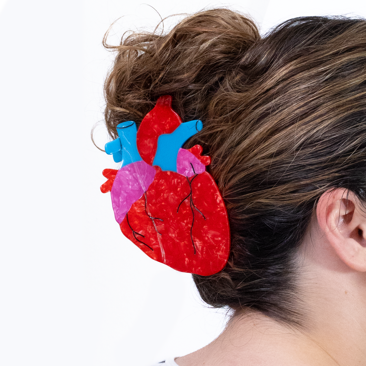 The mega anatomical heart hair claw shown in a persons hair, on a white background