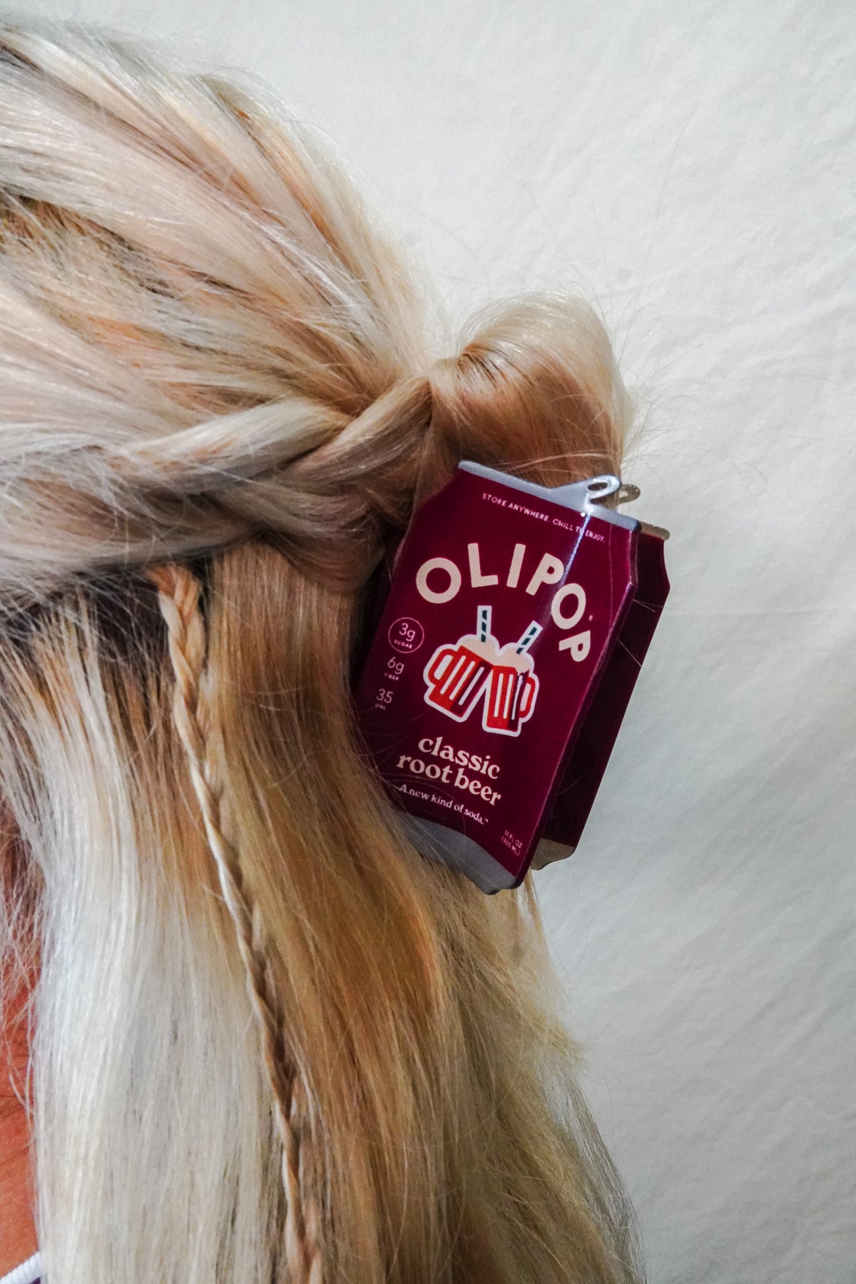 A close-up of a person's blonde hair styled in a half-up bun with a OLIPOP Classic Root Beer hair claw clipped into the hair 